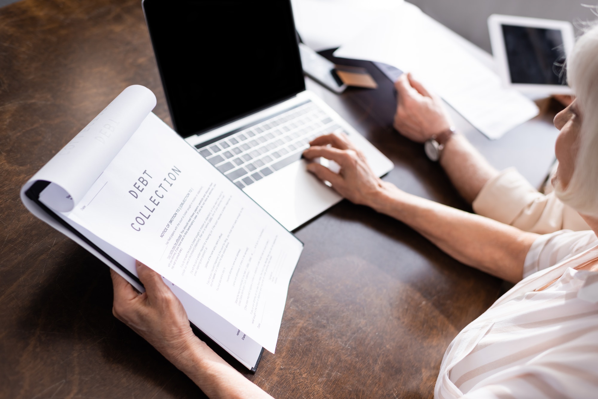 Selective focus of woman using laptop and holding papers with debt collection lettering near man at